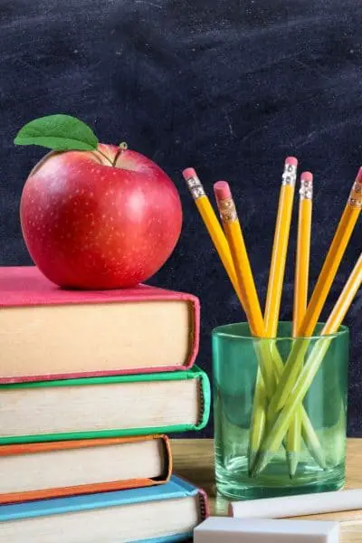 A pile of books with an apple on the top and a jar of pencils next to it.