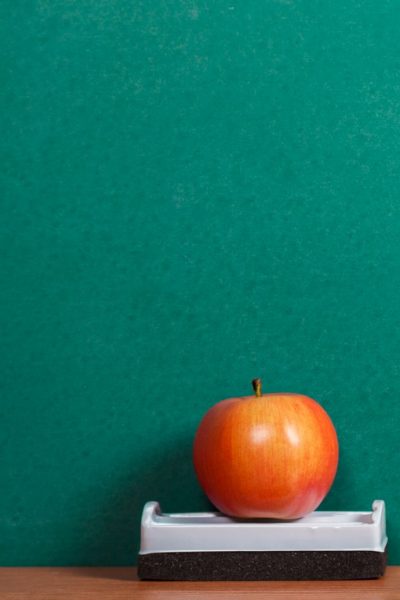 An apple on a blackboard eraser next to the blackboard.