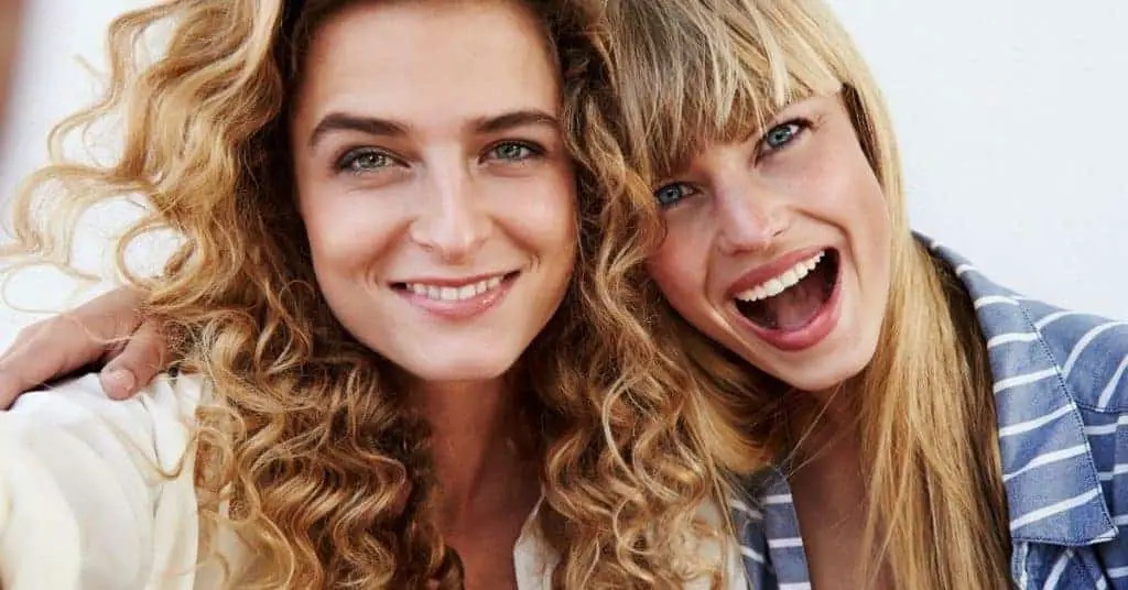 two female colleagues smiling at the camera, connecting as part of their self care at work