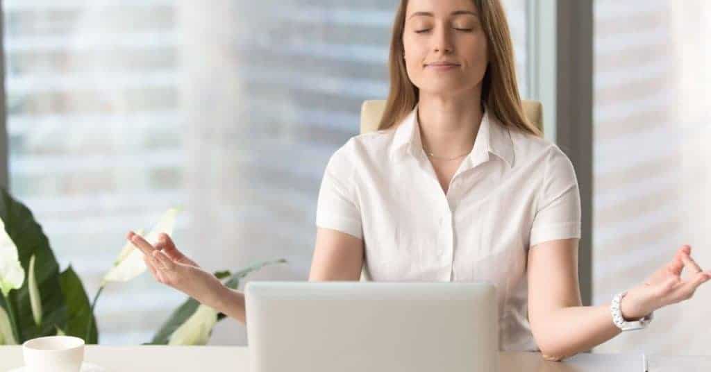 Woman with her eyes shut and smiling, setting her intentions between tasks at work as part of her self care at work activities.