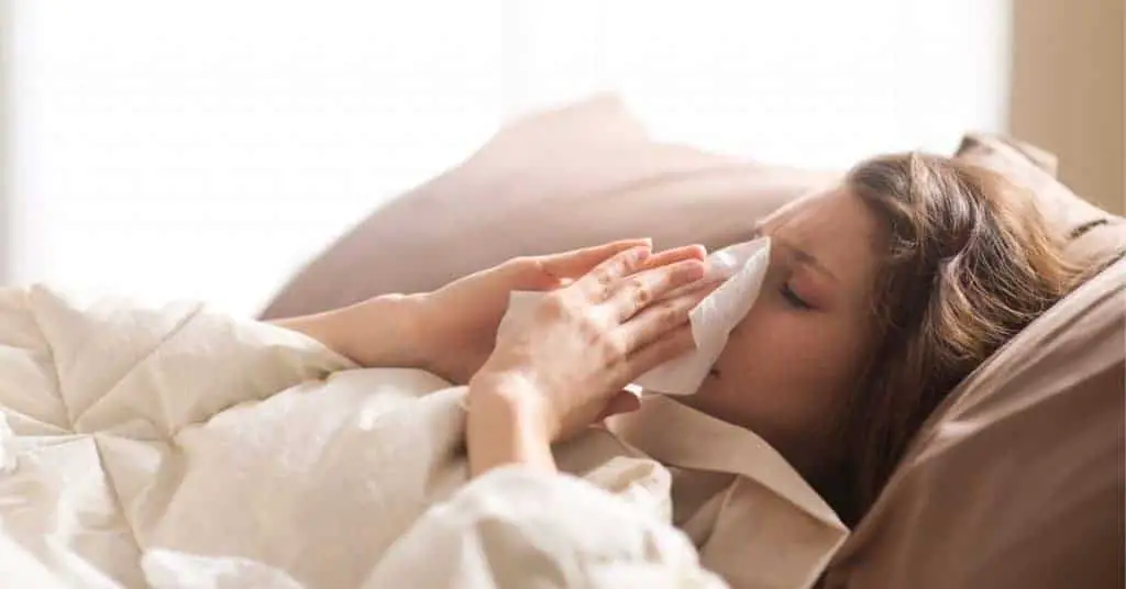 woman sick in bed wiping her nose with a tissue