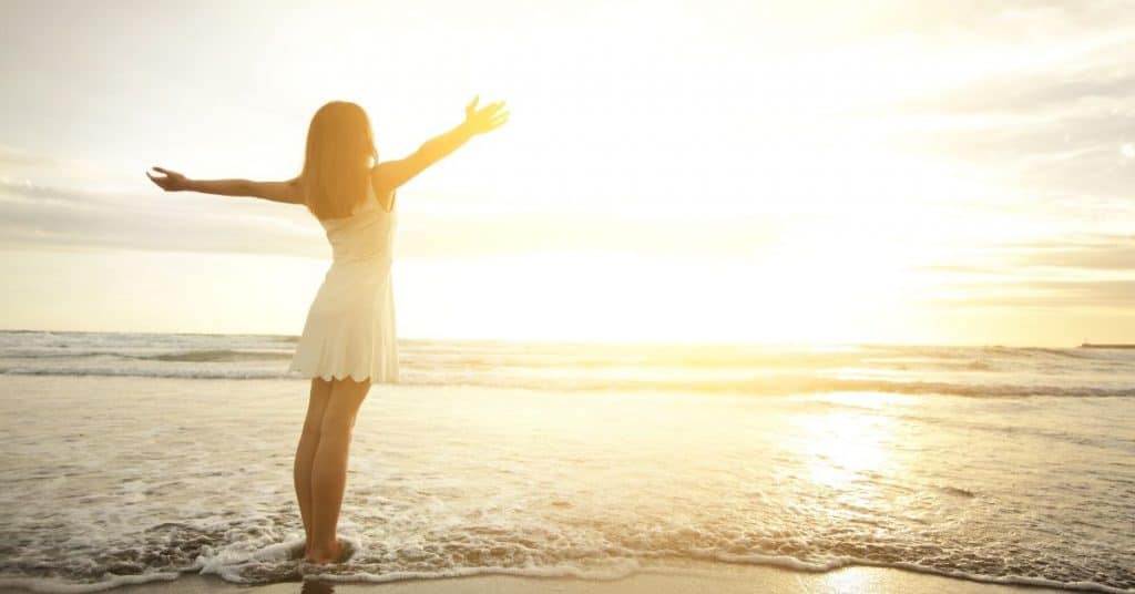 Woman standing in the sea looking at the sunset.