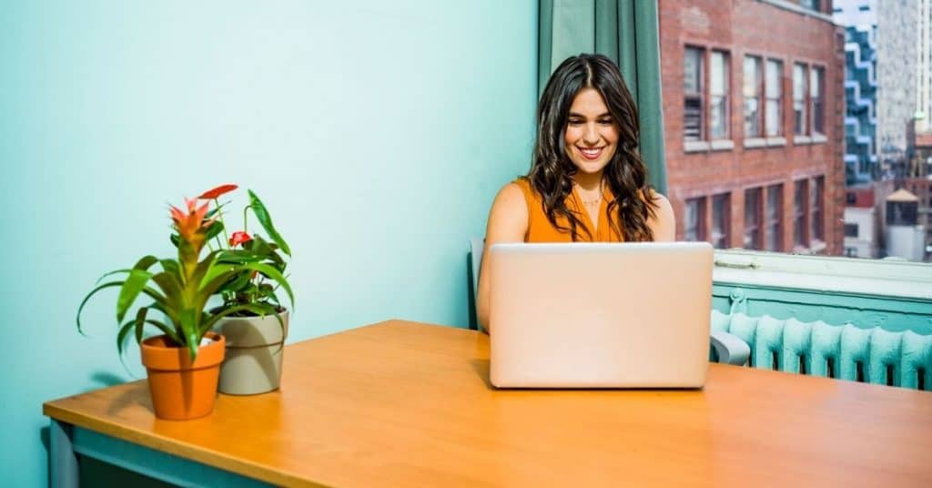 Woman working on a laptop with a mint green background.