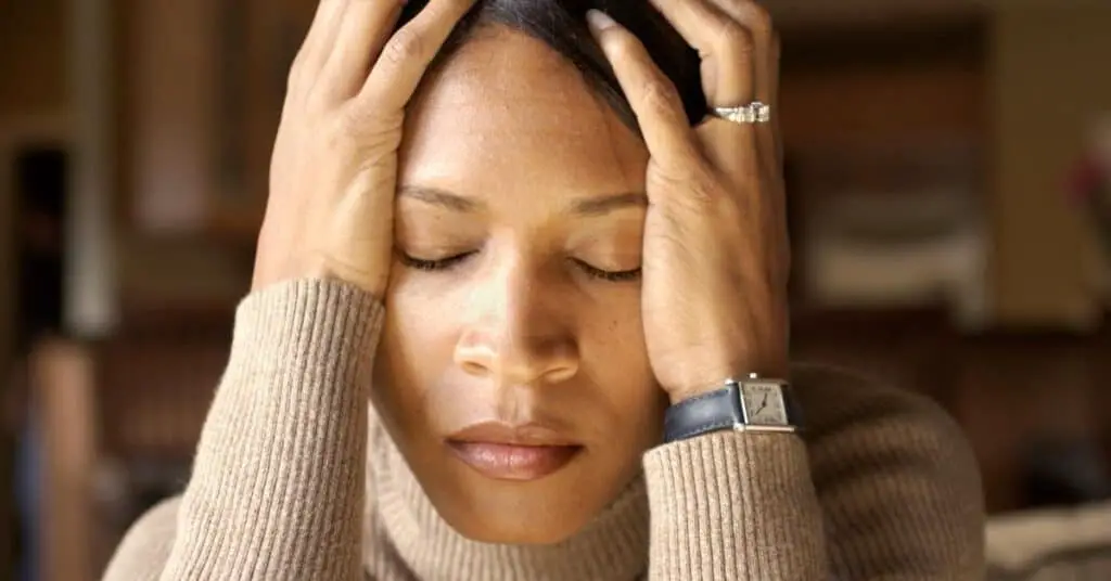 Stressed looking woman with her head in her hands about to create a stop doing list.