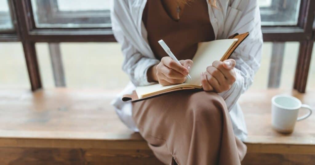 Woman doing a brain dump in a notebook following the strategy of what to do when you fee overwhelmed.