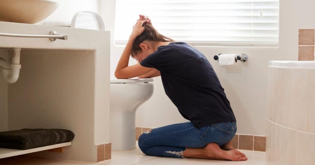 Pregnant teacher with her head over a toilet.