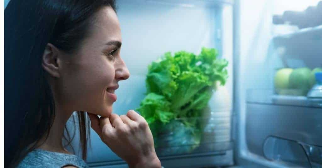 woman looking inside fridge wondering what time she should stop eating at night